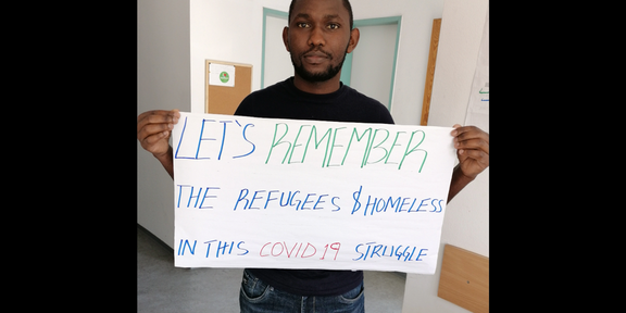 SPRING Remember The picture shows a SPRING student and a poster that reads "let's remember the refugees and homeless in this Covid19 struggle."