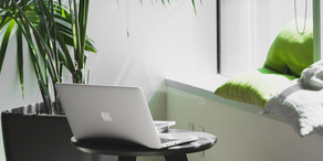 Ein kleiner gemütlicher Arbeitsbereich mit Sitzgelegenheit, Pflanzen und einem Tisch, auf dem ein Laptop platziert ist.