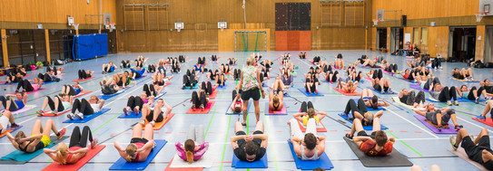 People lying on a mat and doing sports in big gym