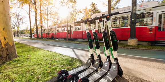 Im Hintergrund fährt eine Straßenbahn und im Vordergrund sind E-Scooter platziert.