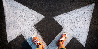 Füße auf weißen Pfeilen auf Asphaltstraße.