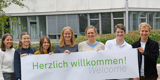 Studierende stehen mit einem Herzlich Willkommen-Banner vor dem GB3.