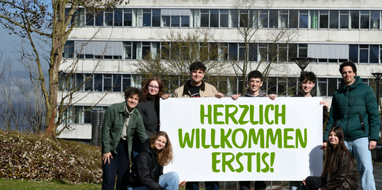Studierende stehen mit einem Herzlich Willkommen-Banner vor dem GB3.