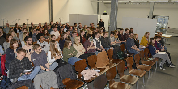 Studierende sitzen auf Stühlen und hören gespannt einem Vortrag zu.