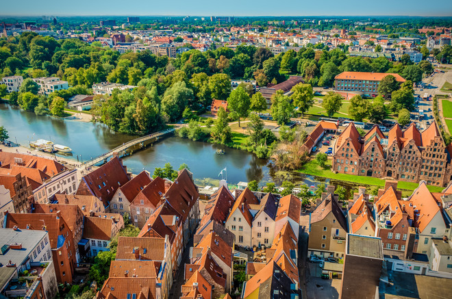 Lübeck aus der Vogelperspektive auf der man Wasser, Haussiedlungen und Wälder sehen kann.