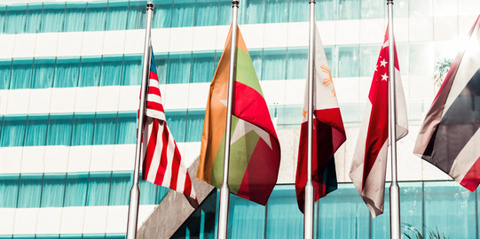 Five flags of countries hang side by side on a pole.