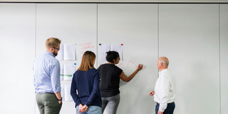 Eine Gruppe von Menschen steht vor einer Wand und notieren Stichwörter.