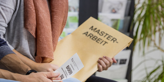 Mensch mit Master-Arbeit-Umschlag sitzt im Warteraum.