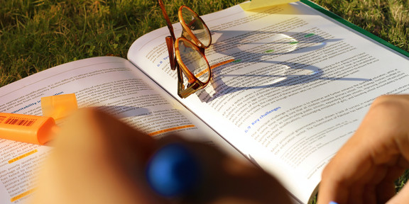 Buch liegt auf einer Wiese mit enier Lesebrille und Notizen.