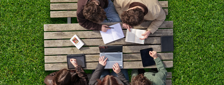Studierende werden von der Vogelperspektive beim arbeiten draußen an einem Tisch gezeigt.