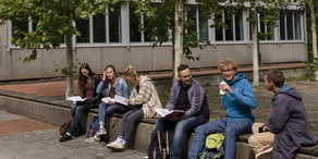 Studenten sitzen auf einer Mauer und tauschen sich aus.