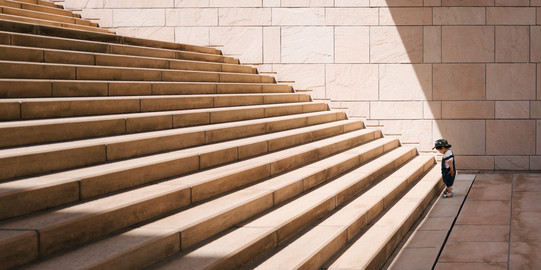Kleines Kind steht vor langer Treppe mit großen Stufen.
