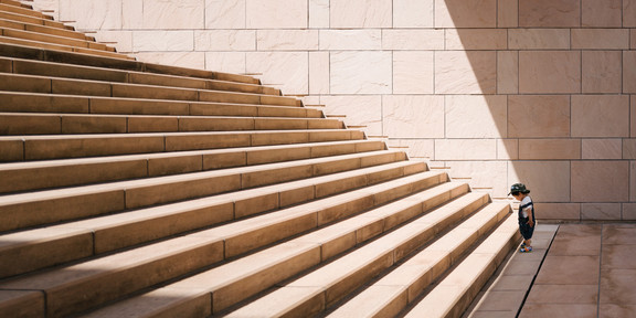 Kleines Kind steht vor langer Treppe mit großen Stufen.