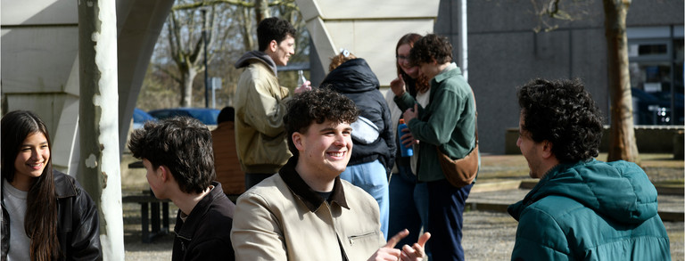 Studierende sitzen draußen am Campus Süd und unterhalten sich.
