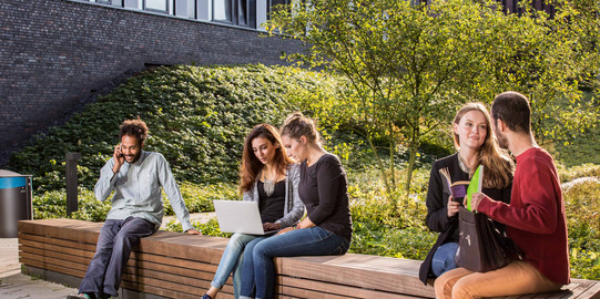 Studierende sitzen auf einer Sitzgruppe hinter dem neuen Physikgebäude