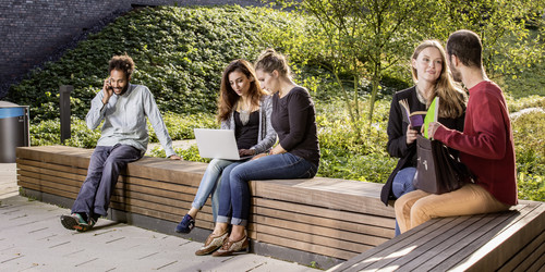 Studierende sitzen auf einer Sitzgruppe hinter dem neuen Physikgebäude
