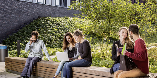 Studierende sitzen auf einer Sitzgruppe hinter dem neuen Physikgebäude