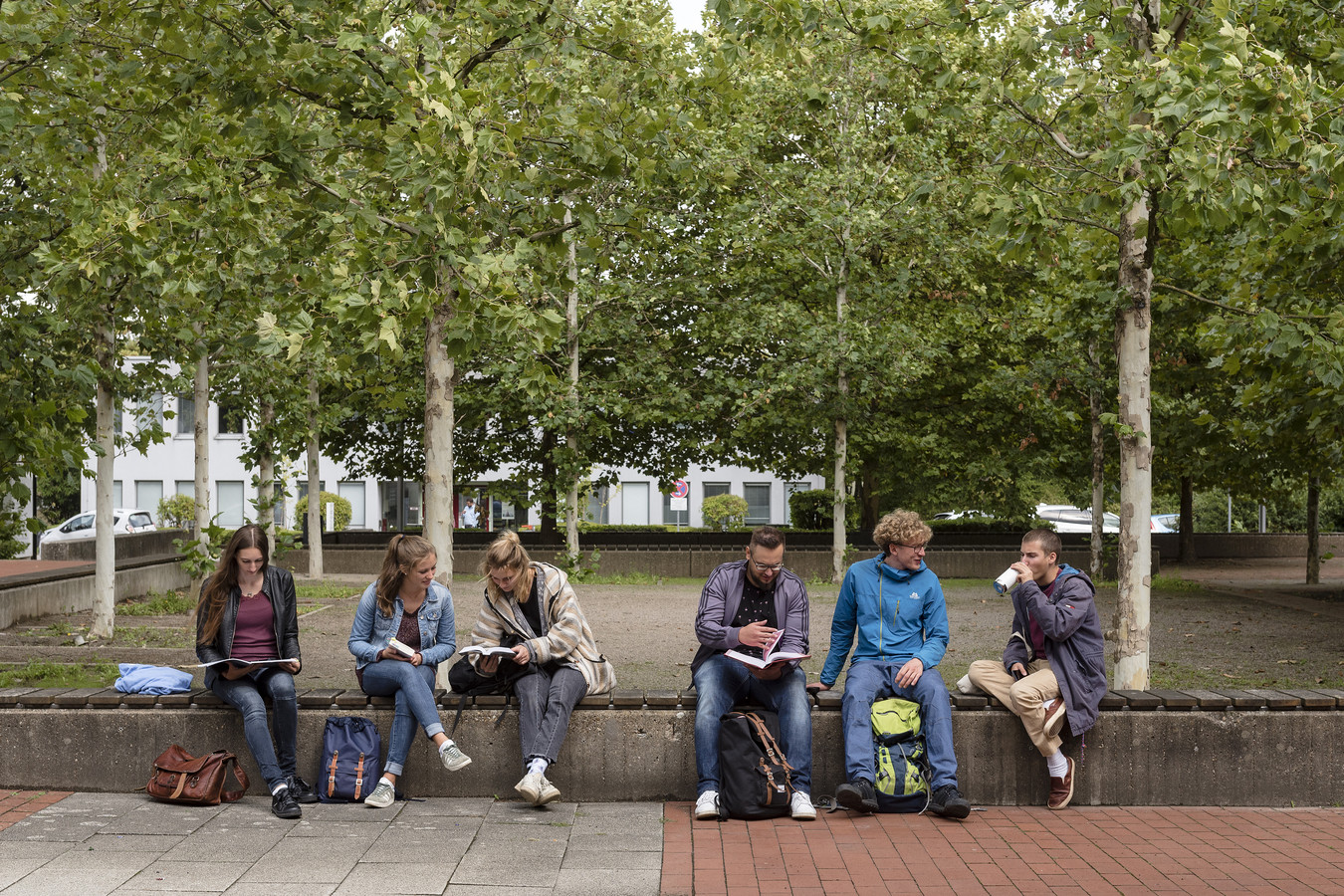Students are sitting on a long bench, holding books and talking to each other.