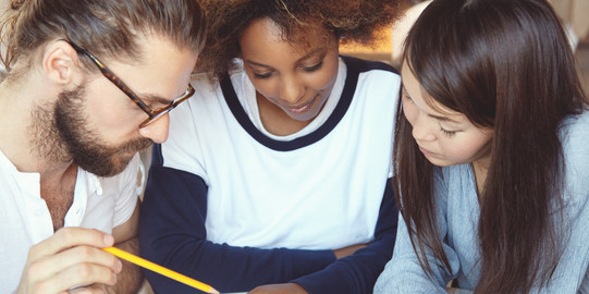 Three students put their heads together over documents.