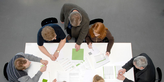 Besprechungssituation Studenten und Professoren Studierende und Dozierende sitzen gemeinsam an einem Tisch und arbeiten.