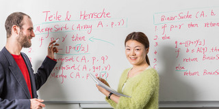 Students at a whiteboard Two people in front of a whiteboard. One is holding a red pen, the other a notepad.