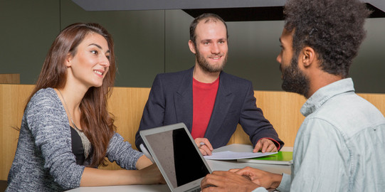 Three students sit opposite each other and they are talking.